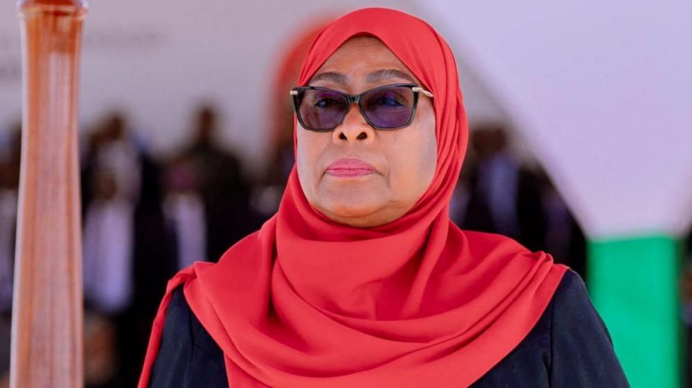 A close-up of Samia Suluhu Hassan wearing dark glasses and a red headscarf.