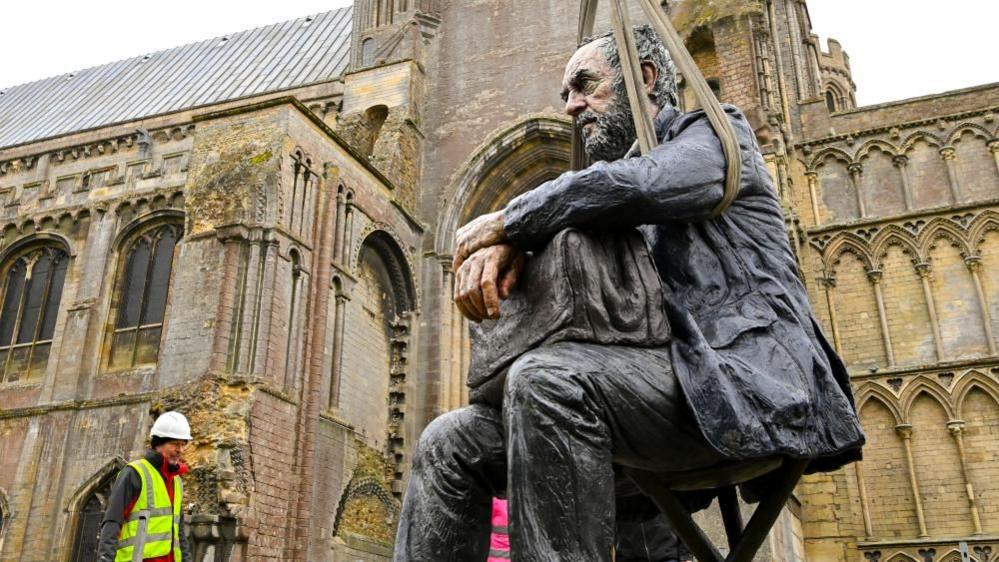 Man watching sculpture being lifted by hoist