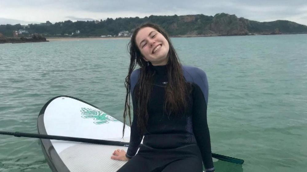Lily is pictured before her illness. She is resting on a paddleboard in the sea.