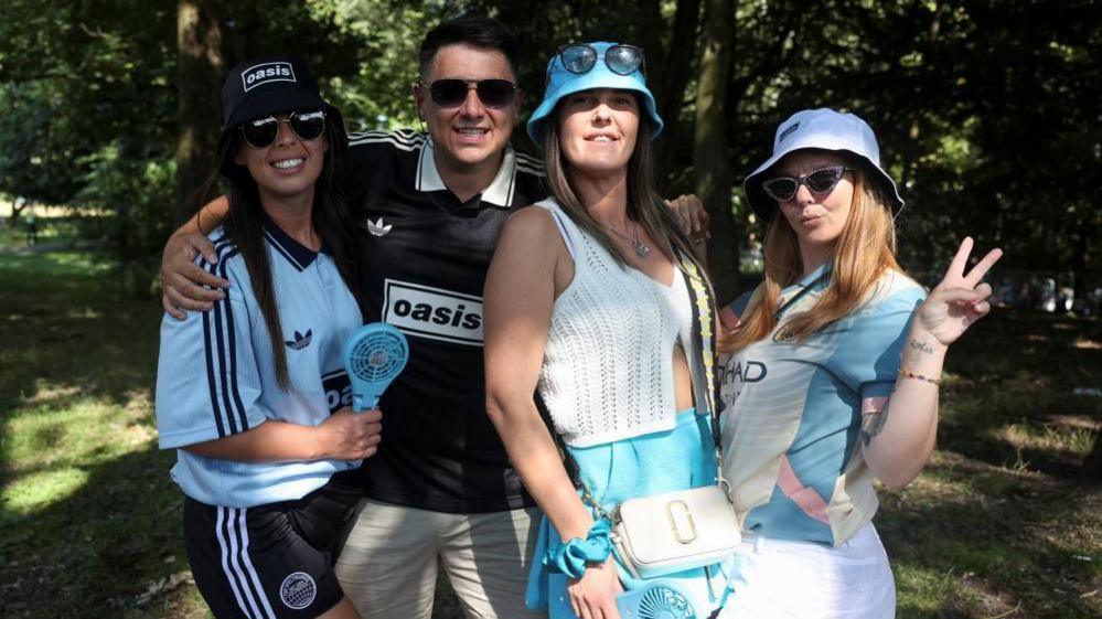 Three out of four Oasis fans wear bucket hats and are holding fans at Heaton Park