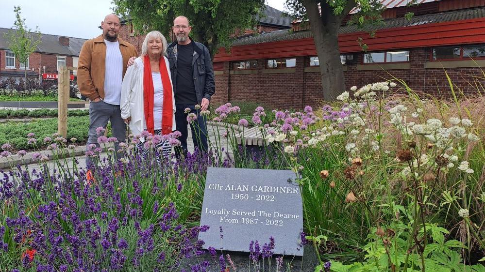 Three people stand behind a plaque