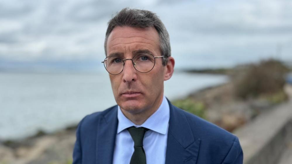 Andrew Muir, a man with grey hair, glasses, a navy suit, blue shirt and dark tie.