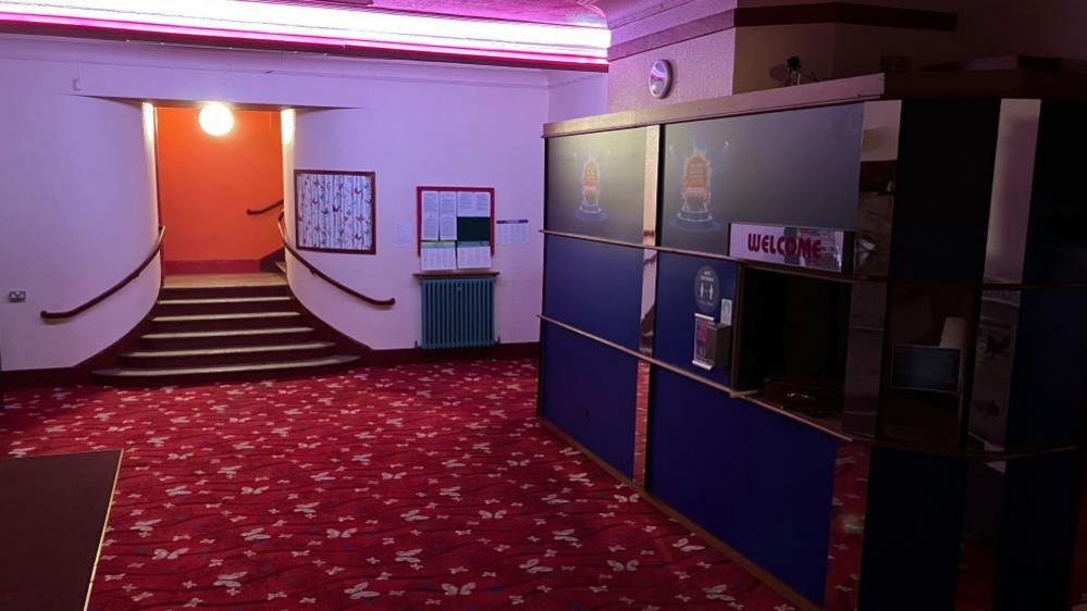 The entrance hall to the bingo hall, with a red patterned carpet and purple walls. in the distance a small staircase to an entrance.