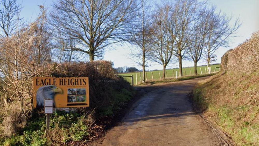 A Google maps image of the orange Eagle Heights sign on a country road leading up to the centre with fields in the distance and hedgerows lining the road