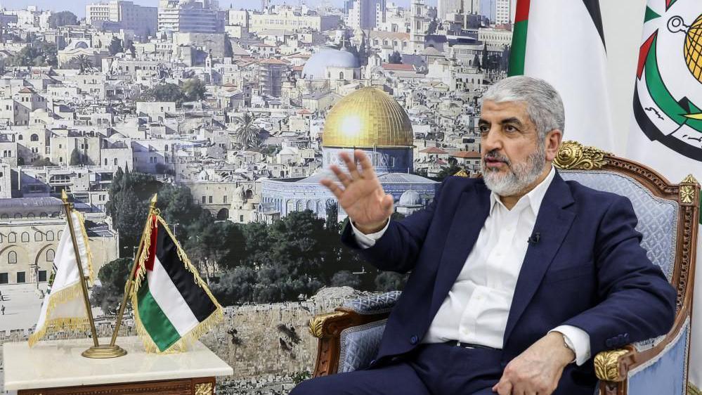 Khaled Meshaal sits in a chair in Doha beside a large picture of Jerusalem