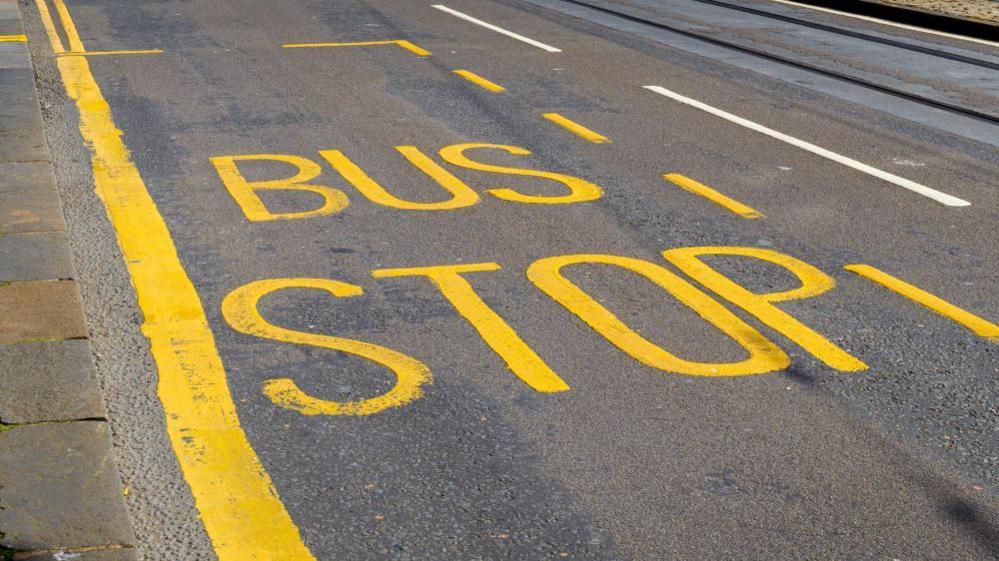 Yellow markings on the road spell out "bus stop". 