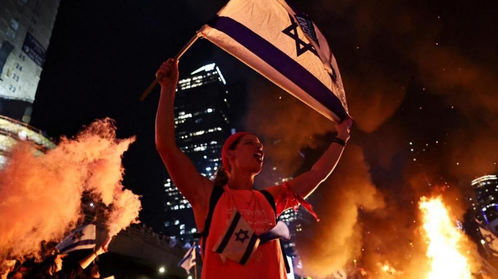 A person holds an Israeli flag as people demonstrate after Israeli Prime Minister Benjamin Netanyahu sacked his defense minister, Yoav Gallant, citing lack of trust, in Tel Aviv, Israel November 5, 2024.