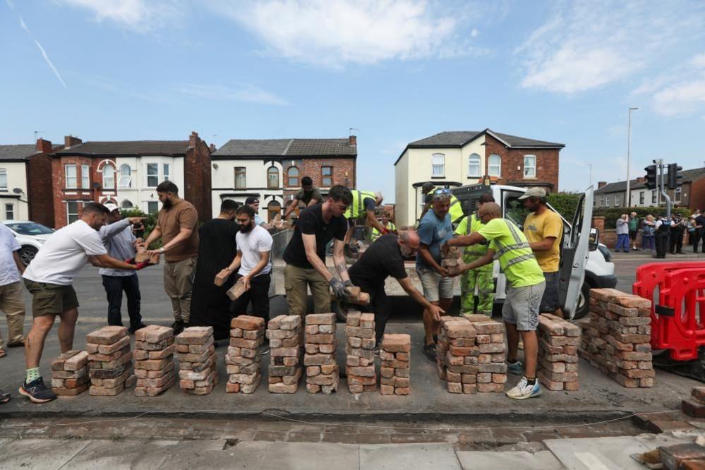 Volunteers with piles of bricks rebuild the fence outside Southport Islamic Society Mosque, after a violent protest