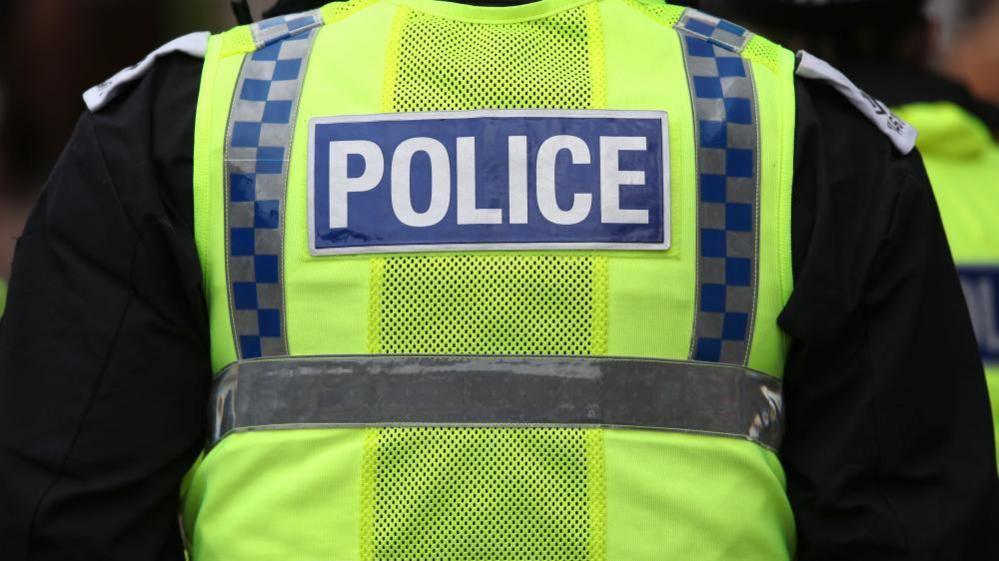 The back of a police officer in a hi-vis police vest, with the word POLICE stitched into the back.