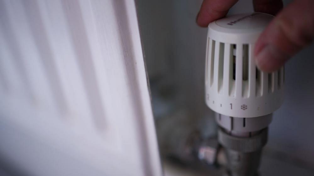 Hand adjusting a thermostat on a radiator.