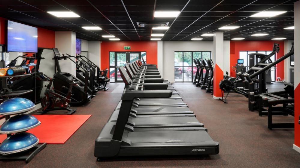 The picture shows the newly refurbished gym at the National Badminton Centre in Milton Keynes. Decorated in black and red colours the gym features a row of treadmills and other workout equipment. 