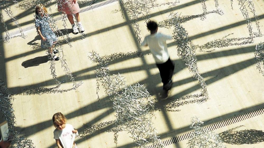 Children walking amongst figures made up of silver steel bars.