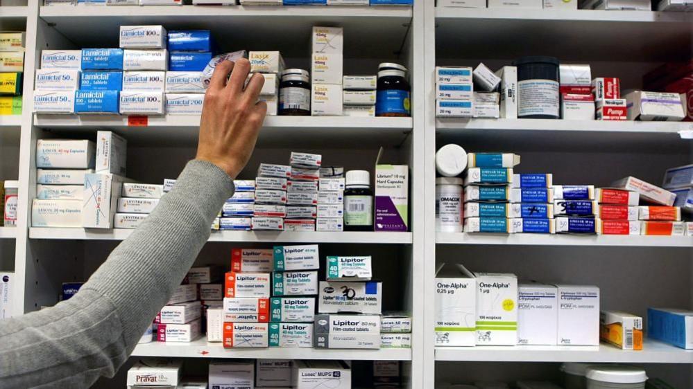 Hand reaches towards shelves stocked with boxes of tablets