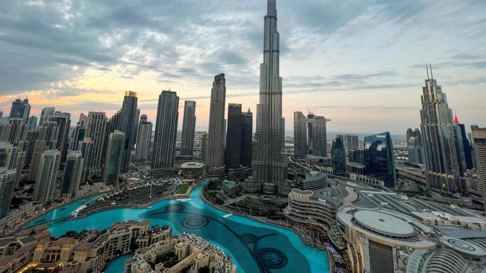 A view of the Dubai skyline backing onto a brightening sky featuring several skyscrapers and a man-made canal full of glistening blue water