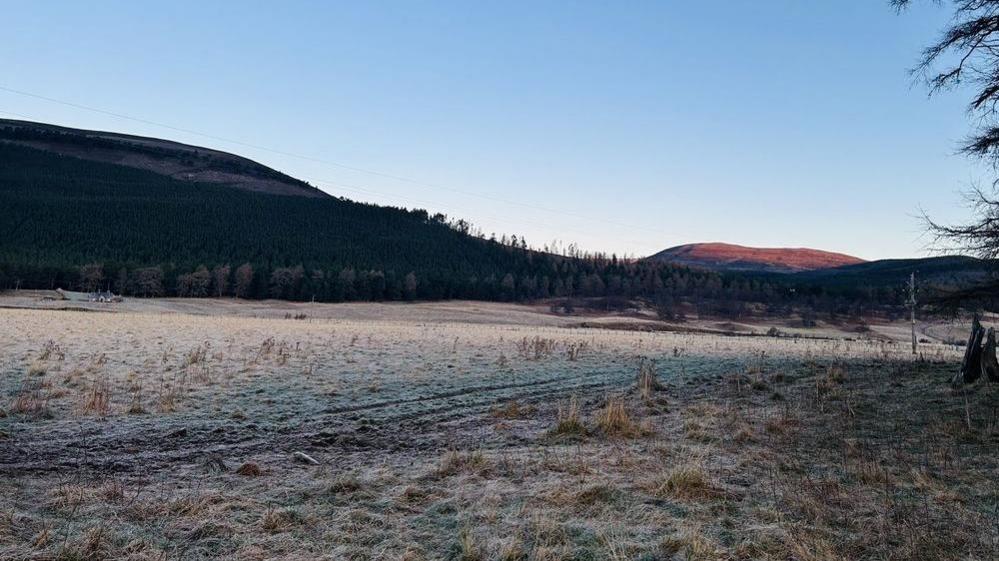 A field is covered in a dusting of icy snow with hills in the background. 