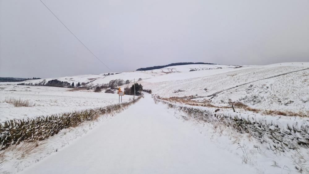 A road with stone fences on either side is covered in a thick layer of snow