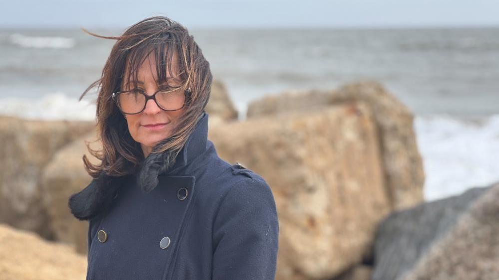 Lorna Bevan with coastal defence blocks behind her in soft focus, with the sea in the background