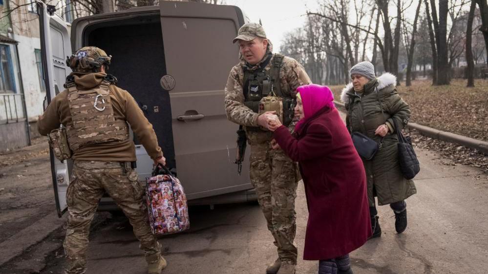 Two men in combat fatigues escorting two elderly women to a van in the Ukrainian town of Pokrovsk