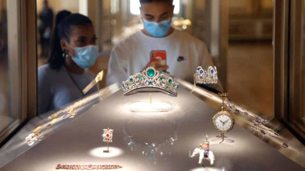 Visitors wearing face masks look at the Duchess of Angouleme's Diadem exposed in a window displayed in the Apollo gallery in the Louvre Museum