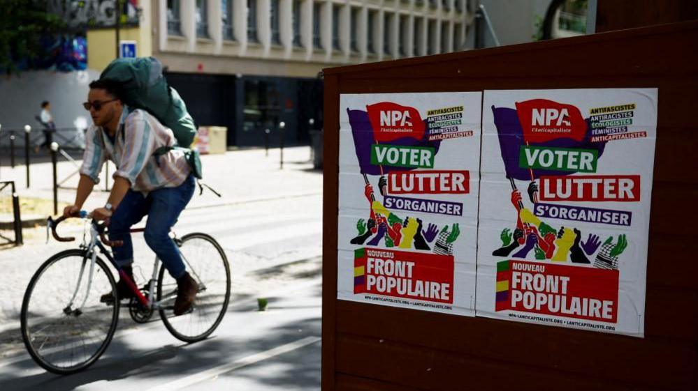 man on bike rides past posters for New Popular Front