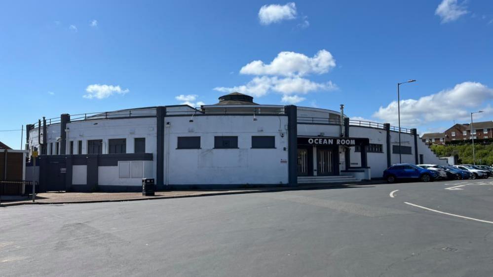 The Ocean Room is an Art Deco rotunda building, painted grey and white. It features steps up to the front doors, above which is the sign reading: "Ocean Room". There are hand rails on the roofline, a symbol of when the roof was used as a public sun terrace.