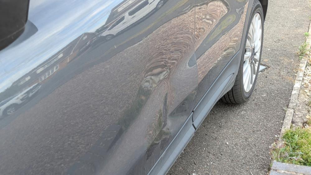 Nearside of grey car, showing large dent consistent with a shoe on the rear door.