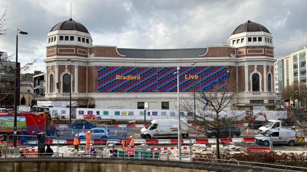 A grand building with a tower at either end and a long digital screen across the centre