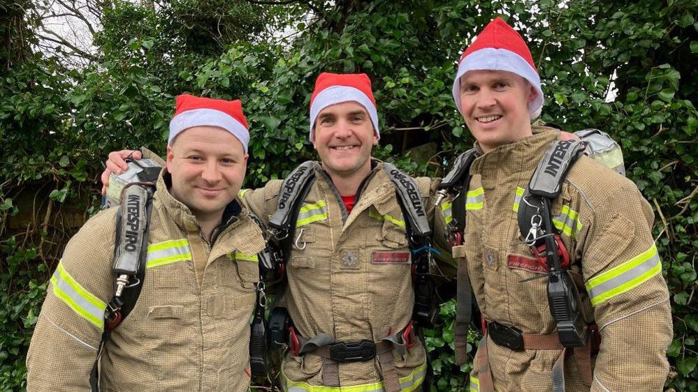 Three firefighters in full gear and santa hats looking at the camera and smiling.