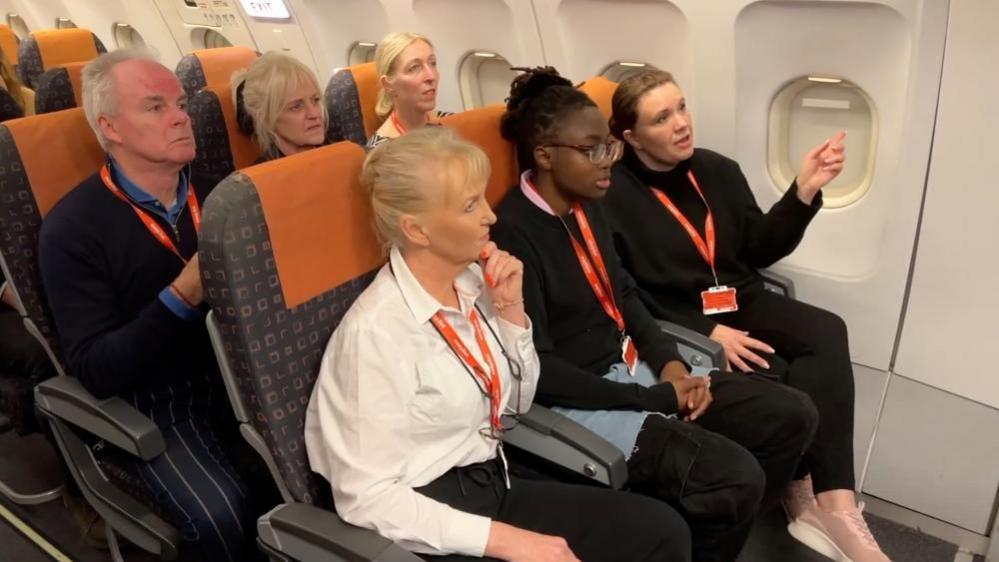 A mixed-age group of trainees sit onboard, while listening to instructions.