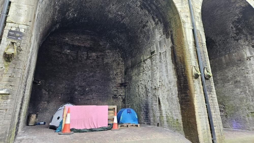 A number of tents belonging to rough sleepers are shown pitched up underneath the arches of a viaduct.