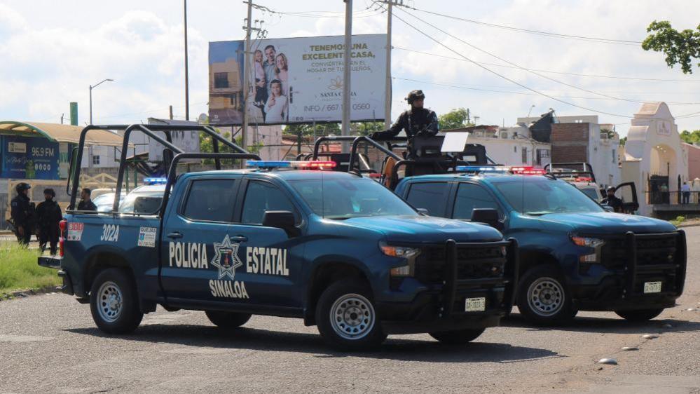 Two trucks emblazoned with the words Sinaloa State Police block a road in Culiacan in this file photo from 11 September 11, 2024. 