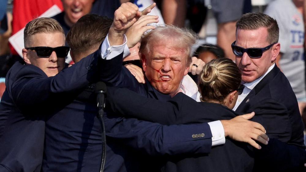 Donald Trump raises his fist after shooting