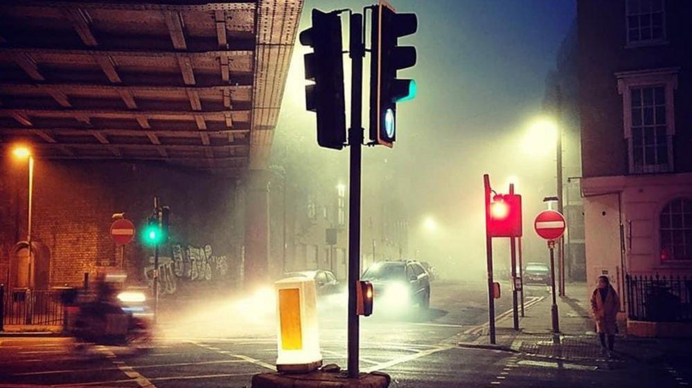 A view of traffic lights, vehicles, pedestrians and graffiti taken in Limehouse at dawn