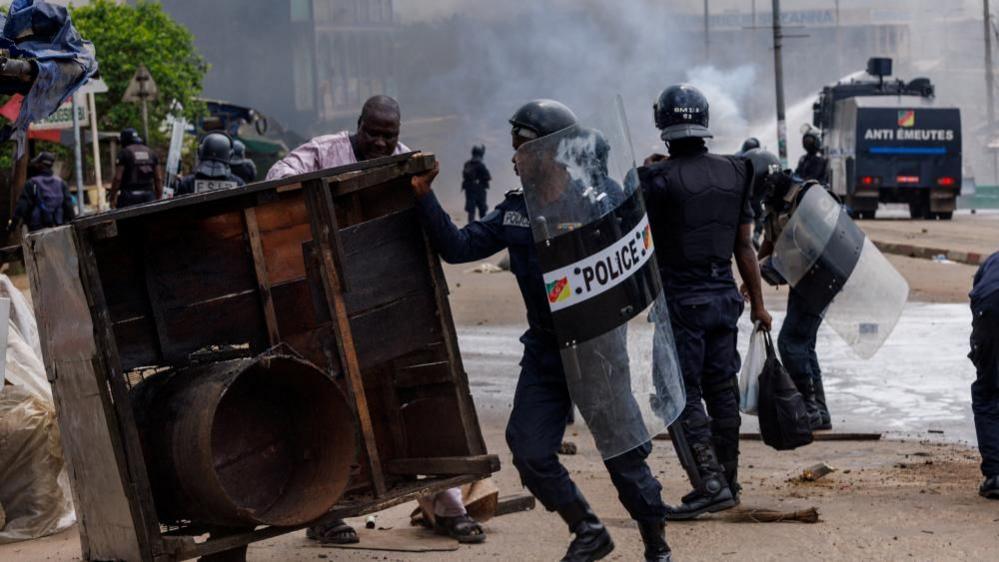 An anti-riot police officer removes a barricade during clashes with supporters of Cameroon presidential candidate Issa Tchiroma, after the Constitutional Council declared President Paul Biya the winner of the October 12 presidential election, in Douala, Cameroon, October 27, 202