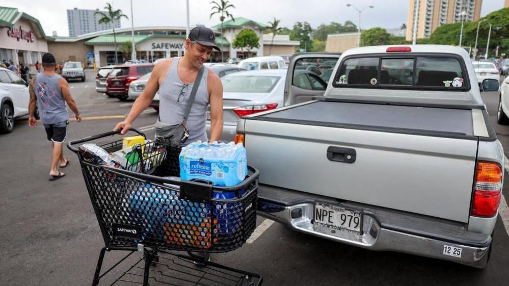 A man at a shopping centre prepares to lift a huge pack of bottled water into his truck.
