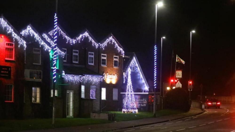 A large property decorated with Christmas lights on the roof and several street lamps with twisted rope braid illuminations