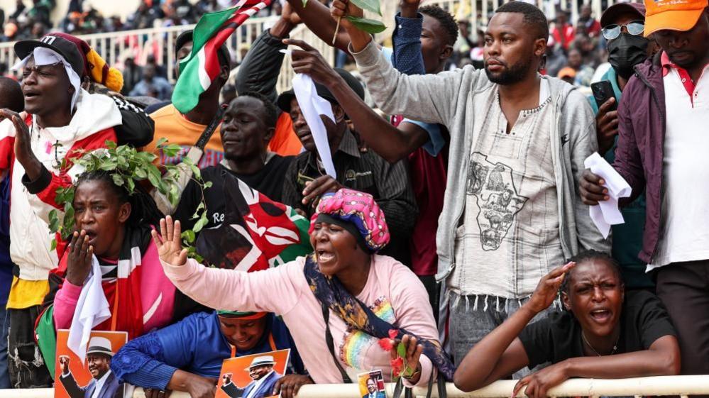 Female and male mourners waiving Kenyan flag and wail at Nairobi's Nyayo Stadium