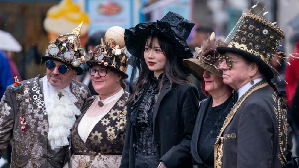 Five people post for a photograph all wearing gothic or steampunk style outfits