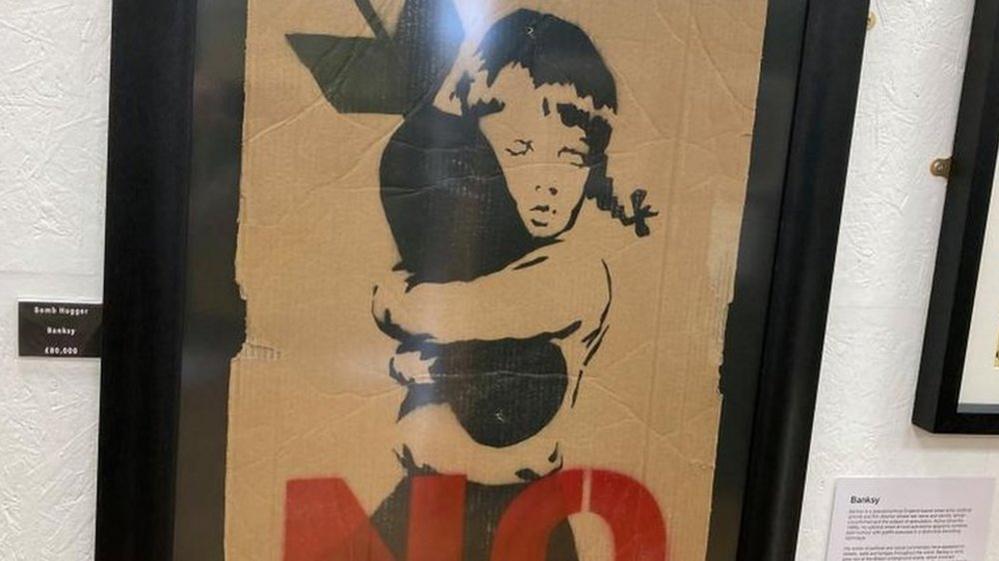 Painting of a child hugging a bomb with the word "NO" in red letters at the bottom