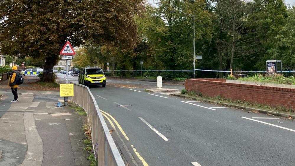 Huntington Road with police tape stretched across it and a police van parked next to it.
