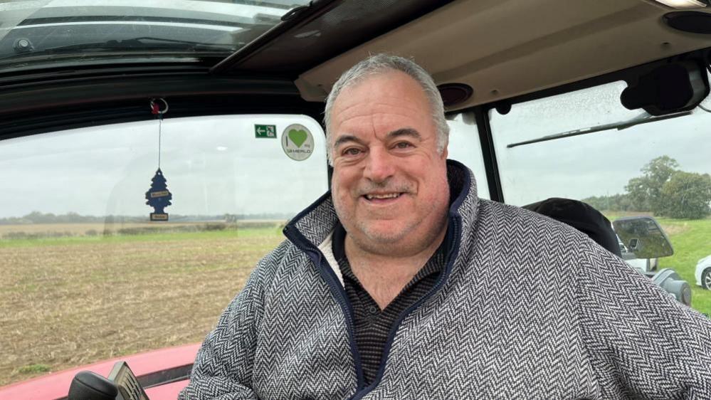 Fred Sharman, wearing a herringbone jacket, sitting in the cab of his fork lift telehandler cab.