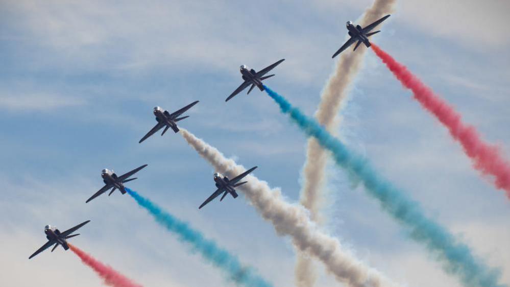 The RAF Red Arrows flying in formation, with red, white and blue vapour trails behind them