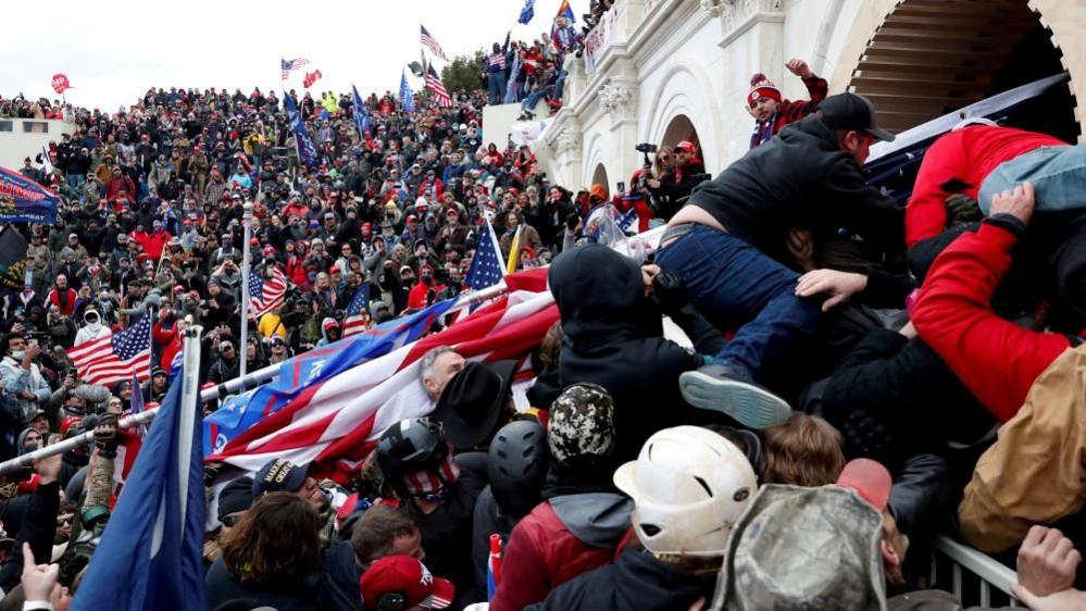 A crowd of Trump supporters surrounding the US Capitol building wave flags and pump fists