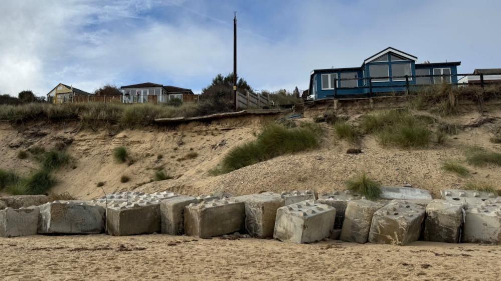 Mark Alden's home is a blue timber-clad property with white window frames, eaves and barge boards. It sits atop the cliff at Hemsby, with sand held up by concrete blocks.