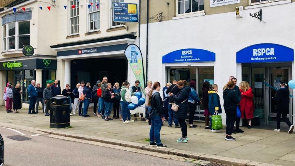 Queue of people on a pavement outside a charity shop