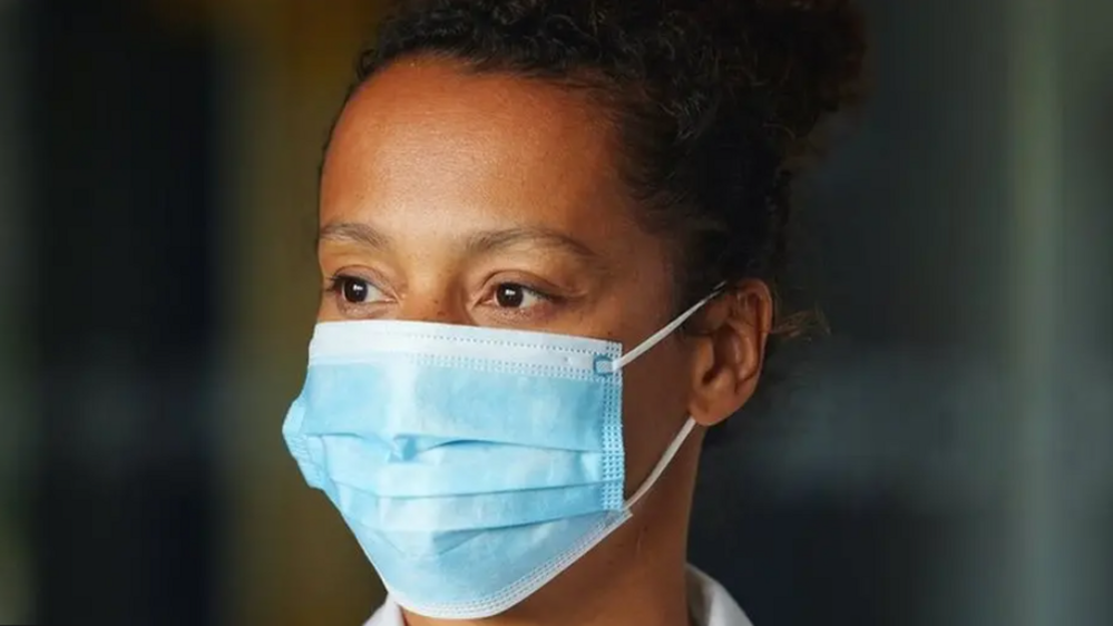 woman with dark curly hair in a bun wearing a blue face mask and looking off to the side