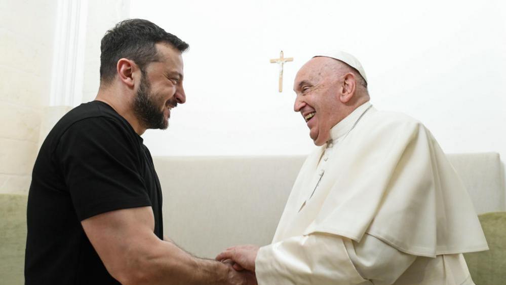 Ukranian President Volodymyr Zelensky and Pope Francis shake hands and smile
