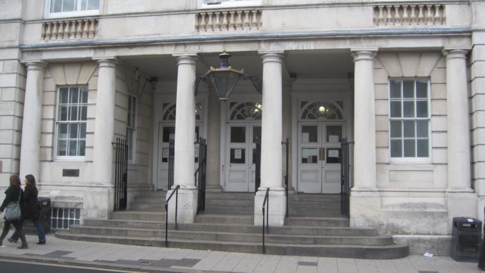 A court building. The court building is made of white brick and has pillars in front of three white doors.