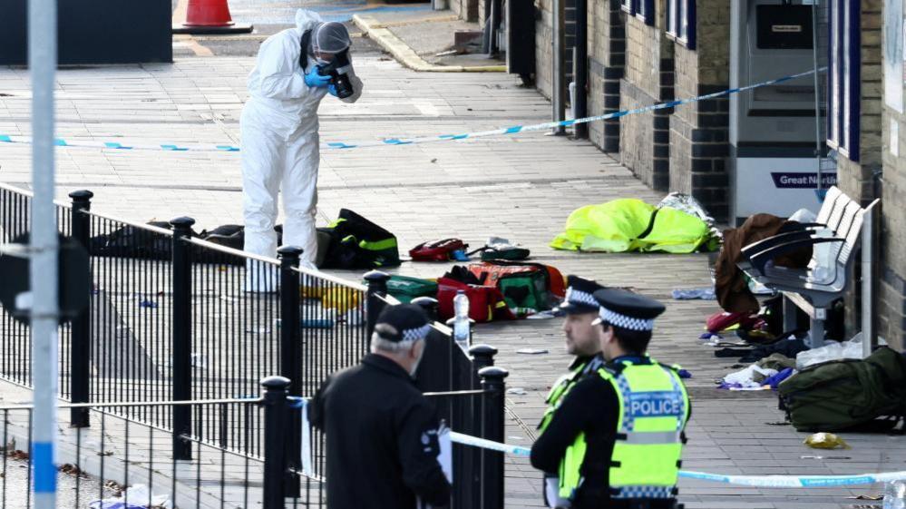 A forensic officer takes pictures at the cordoned-off area at Huntingdon Station, following a series of stabbings on a London North Eastern Railwa