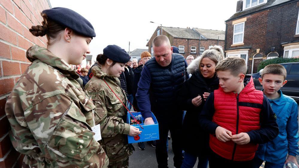 Football fans buy poppies from two women in Army uniforms.